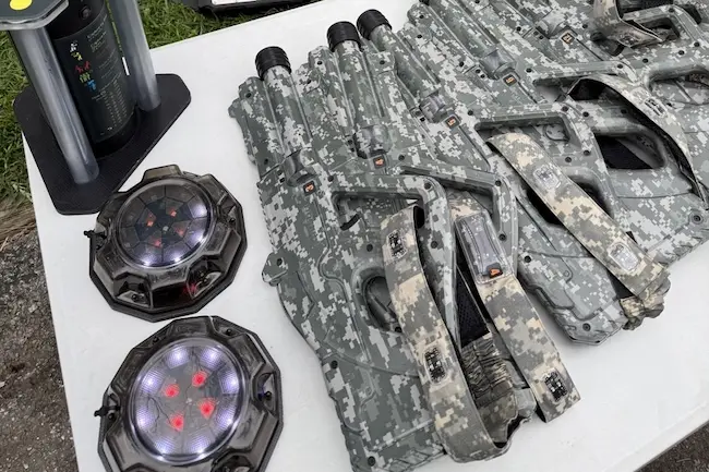 Laser tag guns, tactical vests, and game equipment arranged on a table for an outdoor laser tag event by LaserTagLosAngeles.